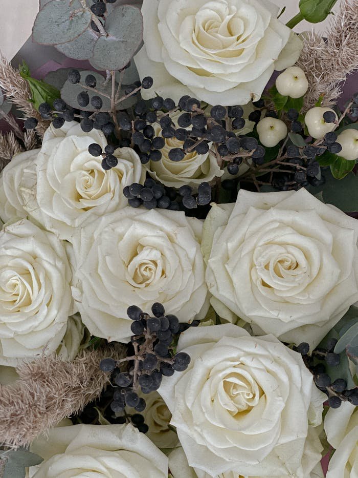 A close-up of an elegant white rose bouquet with black berries, creating a romantic floral arrangement.